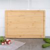 Bamboo cutting board on a kitchen countertop with radishes and cucumbers nearby.
